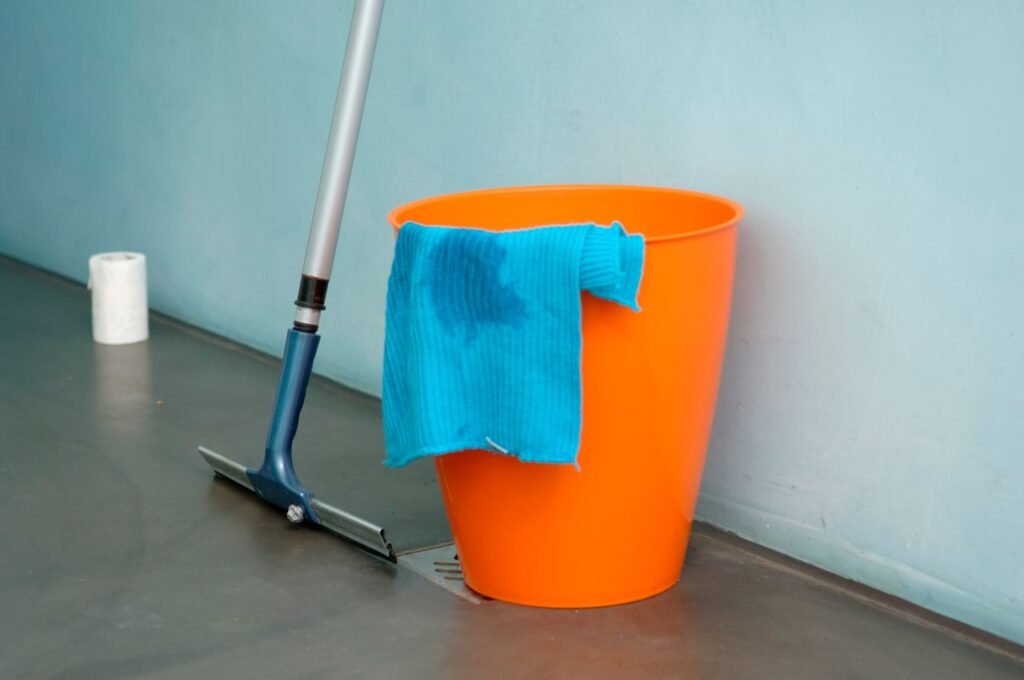 Balde laranja com um pano azul e um rodo de limpeza no chão, exemplificando produtos que falham quando o objetivo é tirar o odor de urina.